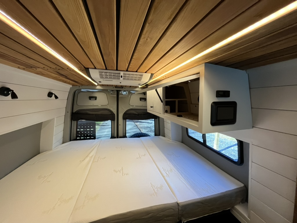 Completed camper van sleeping area beneath a wood ceiling