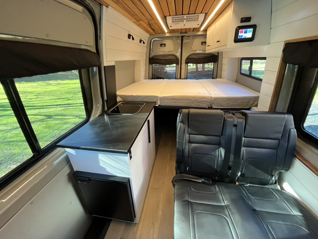 Finished Keystone camper van interior with seating, galley, bed, and wood ceiling