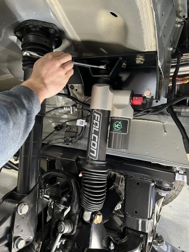 Hands installing a suspension component beneath a van